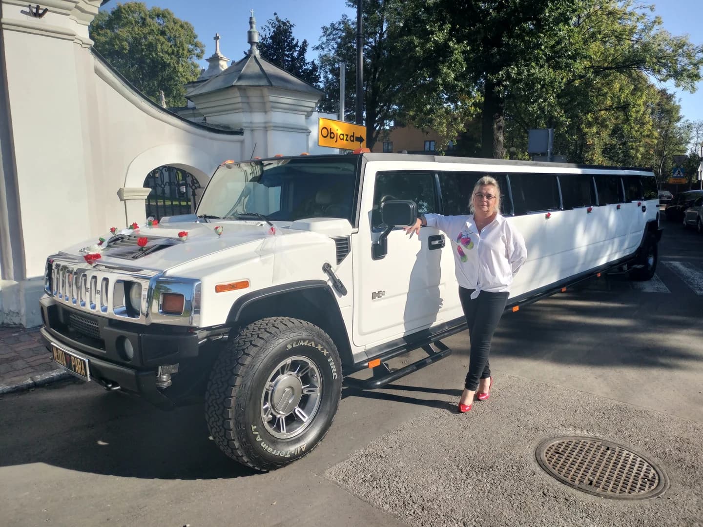 Kobieta w białej koszuli opiera się o długą, białą limuzynę Hummer ozdobioną kwiatami.