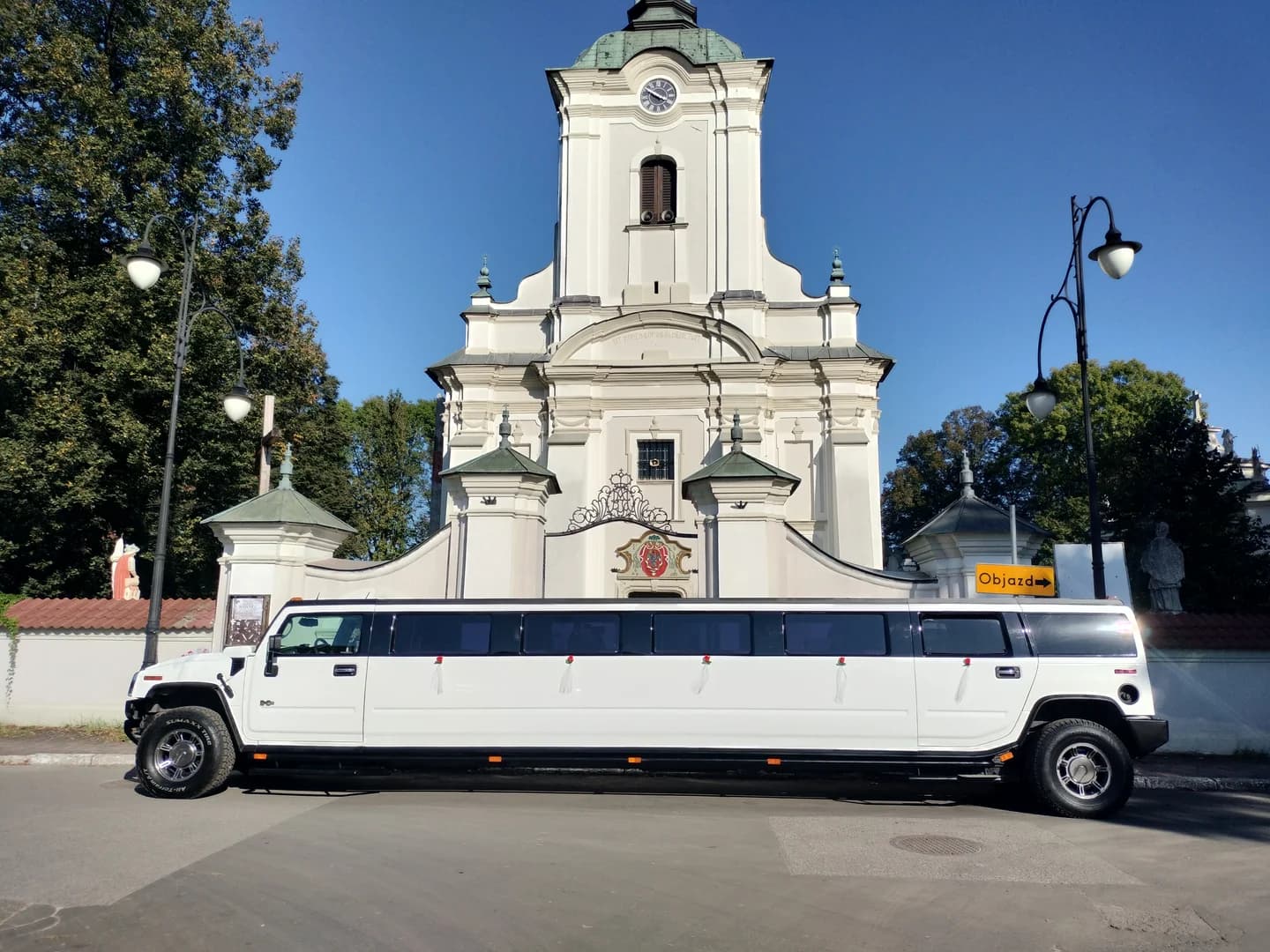 Biała limuzyna typu Hummer zaparkowana na ulicy przed zabytkowym kościołem w słoneczny dzień.