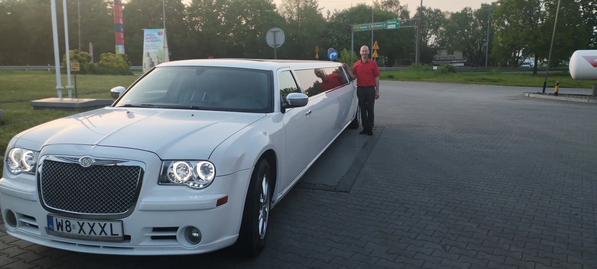 Mężczyzna w czerwonej koszulce stojący przy długiej, białej limuzynie Chrysler.
